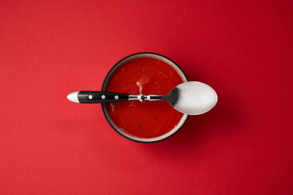 top view of tomato soup in plate and spoon on top of plate on red table