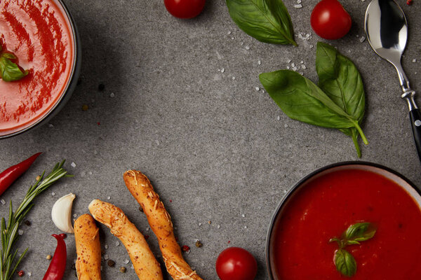 top view of tomato soup, bread sticks and vegetables on grey surface
