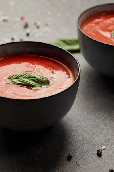 two plates with tasty tomato soup and basil on grey table