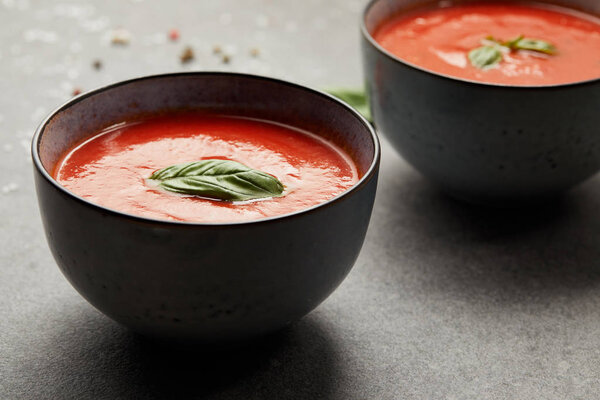 plates with tasty tomato soup and basil on grey table