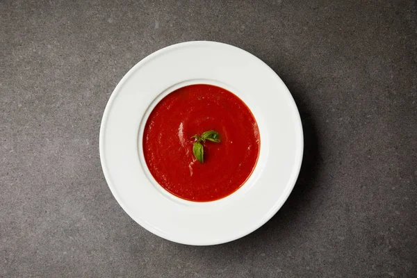 Top view of red tomato soup with basil in white plate on grey table — Stock Image Top View Red Tomato Soup Basil White Plate Grey Table Stock Image