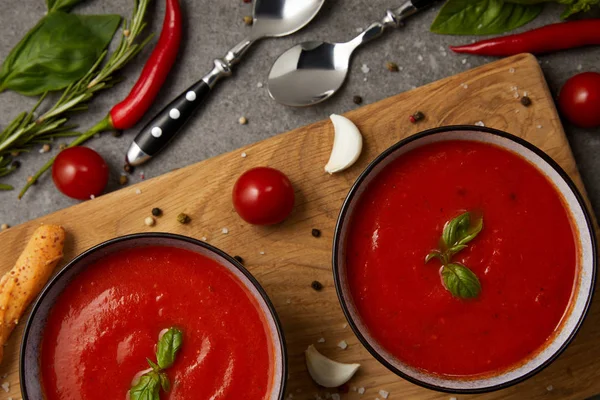 Elevated view of tasty tomato soup in plates on cutting board with vegetables on grey table — Stock Image Elevated View Tasty Tomato Soup Plates Cutting Board Vegetables Grey Royalty Free Stock Images
