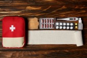Draufsicht auf Verbandstasche mit verschiedenen Pillen, Verband und elektrischem Thermometer auf Holztischplatte
