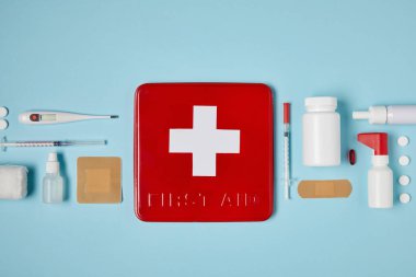 top view of red first aid kit box on blue surface with medical supplies