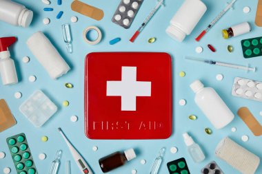 top view of red first aid kit box on blue surface surrounded with different medicines