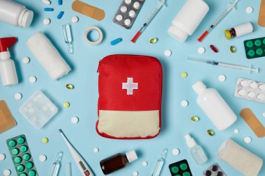 top view of red first aid kit bag on blue surface surrounded with different medicines clipart
