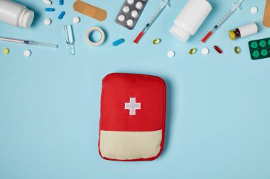 Kırmızı ilk yardım çantasında üstten görünüm farklı ilaçlarla birlikte mavi yüzeyi