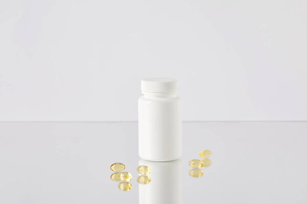 omega fish hat supplement capsules with blank jar on reflective surface and on white