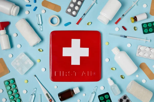 红色急救箱在蓝色表面被不同的药物包围的顶部视图 — 图库照片