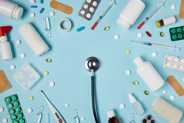 вид сверху стетоскопа, окруженный различными лекарствами на голубой поверхности
