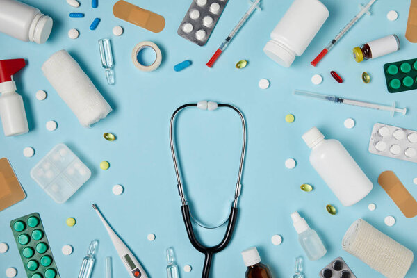 top view of stethoscope surrounded with different medicines on blue surface