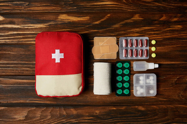 top view of first aid kit composed with various pills and bandage on wooden tabletop