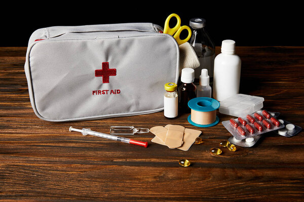 close-up shot of first aid kit with different medicines on wooden tabletop and on black