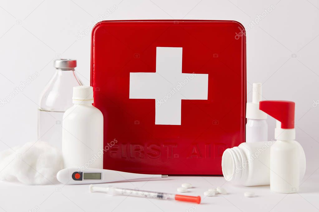 close-up shot of red first aid kit box with different medical bottles and supplies on white
