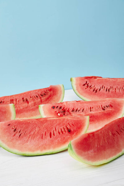 close up view of arranged watermelon slices on white surface on blue backdrop