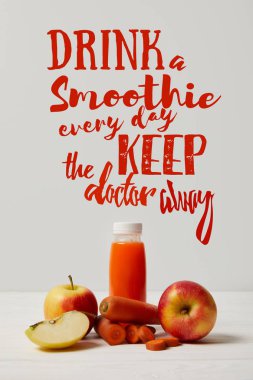 bottle of detox smoothie with apples and carrots on white wooden surface, drink smoothie everyday keep doctor away inscription clipart