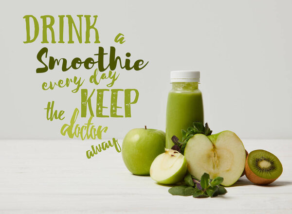 green detox smoothie with apples, kiwi and mint and on white wooden surface, drink smoothie everyday keep doctor away inscription