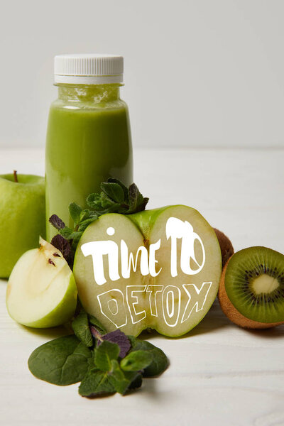 bottle of green detox smoothie with apples, kiwi and mint and on white wooden surface, time to detox inscription
