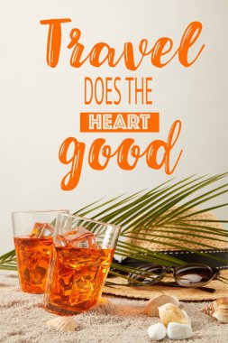 close up view of straw hat, cocktails, seashells, sunglasses and palm leaf on sand on grey backdrop, travel does heart good inscription clipart