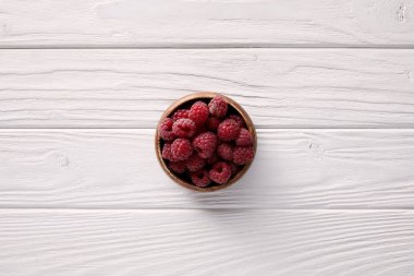 top view of bowl with ripe raspberries on white wooden table clipart