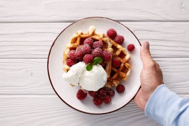 ahududu ve dondurma ile Belçika Waffle tabak Beyaz ahşap masa üzerinde tutan adam resmini kırpılmış