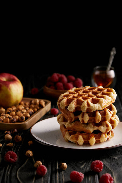 пачка свежеиспеченных бельгийских вафель на тарелке с лесными орехами и малиной на черном деревянном столе
