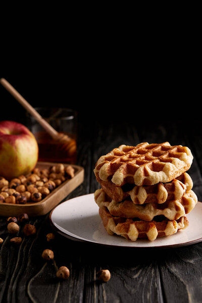 stack of belgian waffles on plate with hazelnuts and apple on black wooden table
