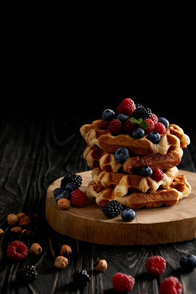 stack of belgian waffles with berries on wooden cutting board on black