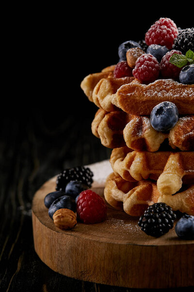 close-up shot of delicious belgian waffles with berries on wooden cutting board on black