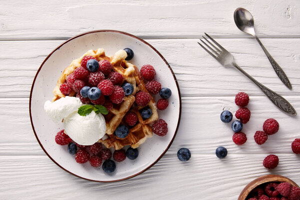 вид на вкусные бельгийские вафли с ягодами и мороженым на белом деревянном столе
