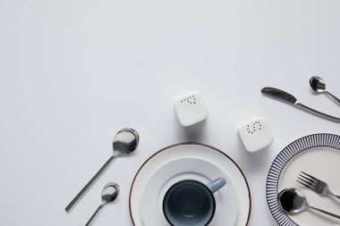 Beyaz masada saltcellar, biber tekeri, kaşık, bıçak, çatal, kupa ve plaketler, üstten görünüm