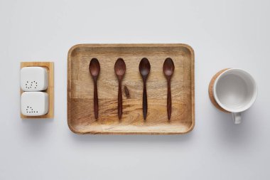 top view of arranged wooden tray with spoons, saltcellar, pepper caster and cup on white table clipart