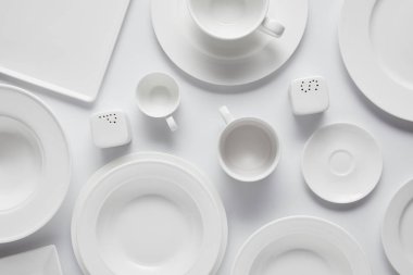 beyaz masa üzerinde çeşitli tabak, kase, saltcellar, biber tekeri ve bardak üstten görünüm