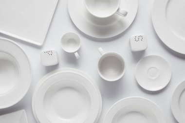 top view of various plates, bowl, saltcellar, pepper caster and cups on white table clipart