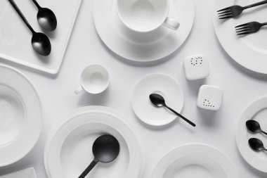 beyaz masa üzerinde siyah kaşık, çatal, salata kaşığı, farklı tabak, kase, saltcellar, biber tekeri ve Kupası üstten görünüm