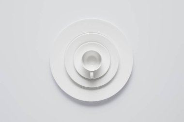 top view of arranged stack of different plates and cup on white table, minimalistic concept clipart