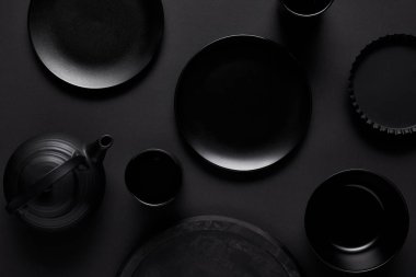 top view of black teapot, plates, bowl, cups, tray and baking dish on black table  clipart