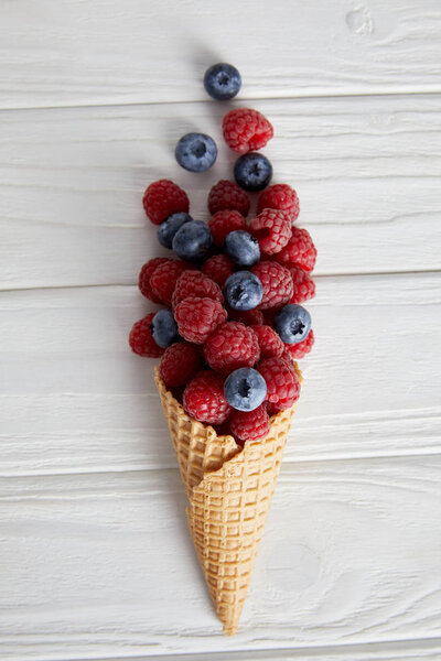 top view of waffle cone with blueberries and raspberries on wooden table 