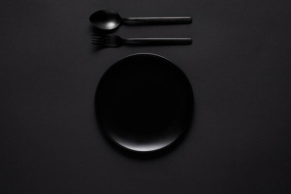 top view of black plate, fork and spoon on black table, minimalistic concept