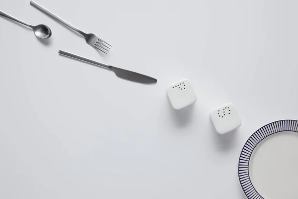 Top view of arranged knife, fork, spoon, pepper caster, saltcellar and plate on white table — Stock Image Top View Arranged Knife Fork Spoon Pepper Caster Saltcellar Plate Royalty Free Stock Photos