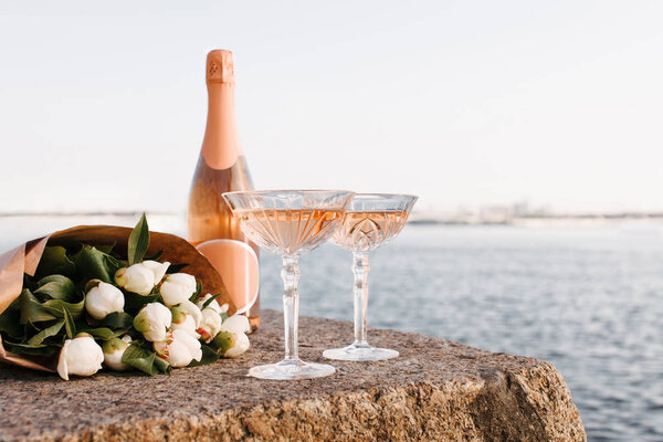 крупным планом два бокала, бутылка шампанского и красивый букет цветов на набережной на берегу реки
