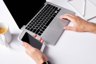 laptop ile çalışma ve smartphone ile boş ekran beyaz yüzeyde tutan adamın kırpılmış atış
