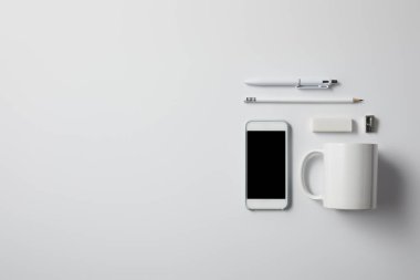 top view of smartphone with various supplies and cup on white surface for mockup clipart