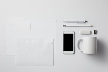 top view of smartphone with various supplies and blank papers on white surface for mockup clipart