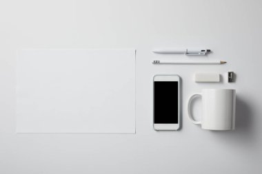 top view of smartphone with various supplies and blank paper on white tabletop for mockup clipart