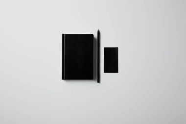 top view of black notebook with pencil and blank business card on white surface for mockup clipart