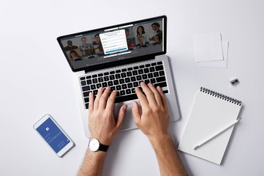 LinkedIn Web sitesinde beyaz yüzey üzerinde işyerinde smartphone içinde ekran ve facebook uygulaması ile dizüstü bilgisayar kullanan adam kırpılmış atış