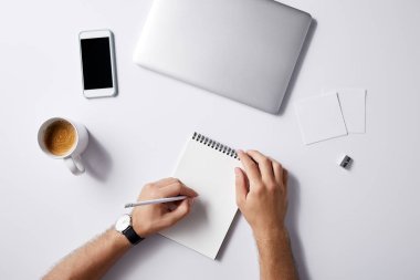 İşyerinde Not defterinizdeki gadget'lar ve kahve fincanı ile mockup için beyaz yüzey üzerinde yazma adam resmini kırpılmış