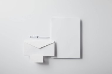 kalem, boş kağıt ve kartvizit ile katmanlı zarf üstten görünüm mockup için beyaz yüzeyi