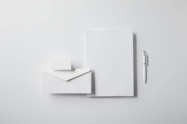 kalem, boş kağıt ve kartvizit ile düzenlenmiş zarf üstten görünüm mockup için beyaz masa üzerinde